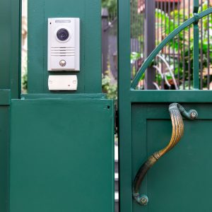 an intercom with a video camera and a microphone for voice communication with a card reader for access by a key card is installed on a green iron gate with handle, close up nobody.